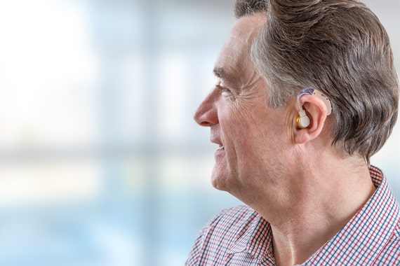 Un senior utilise un appareil auditif et peut réentendre les conversations autour de lui